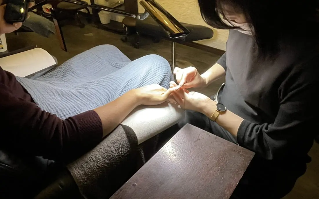 サロンで男性がリクライニングチェアに座り、プロによる丁寧なネイルケアを受けている様子