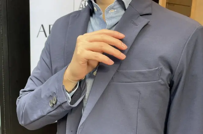 ネイビージャケットとシャツを着た男性が胸元を整えている様子