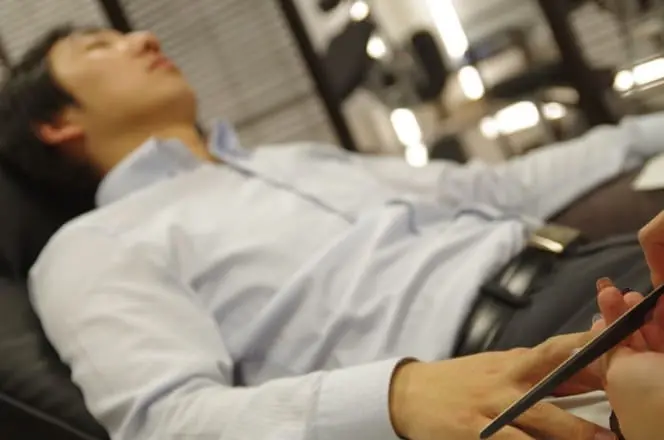 リクライニングチェアに横たわりながら、手元のネイルケアを受けている男性