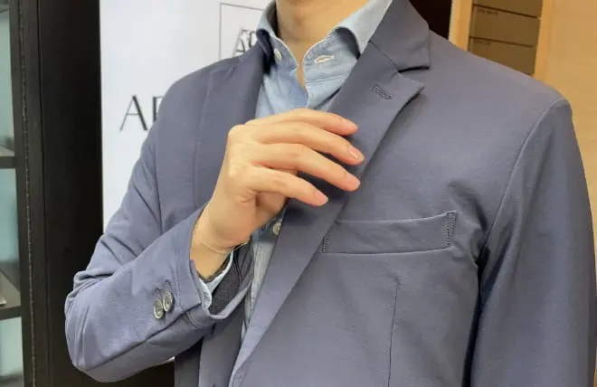 青系のジャケットを着た男性が胸元を整える仕草をしている、身だしなみを意識したシーン