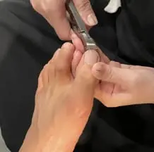 足の爪をニッパーで丁寧に整えているシーンで、専門的なフットケア施術の一環