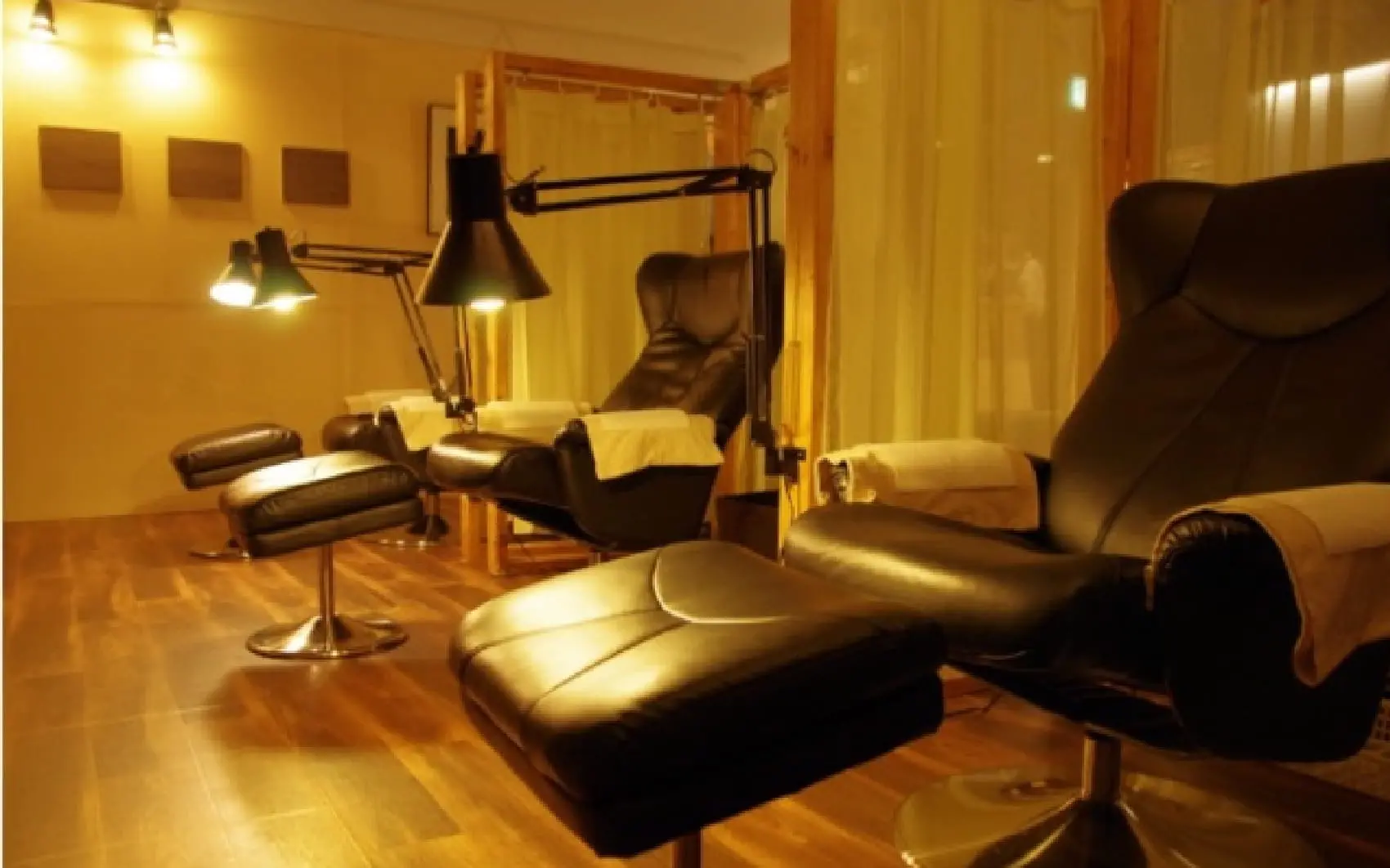 落ち着いた照明の中、リクライニングチェアが並ぶネイルサロンの施術スペース