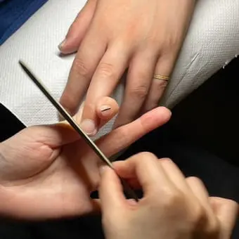 「爪に縦線が入った親指のネイルをケアしている様子」